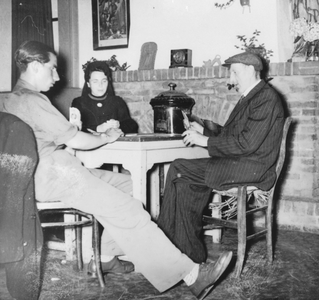 876598 Portret van twee mannen en een Zuster Augustines die aan het kaarten zijn, tijdens een vaderavond in een zaaltje ...